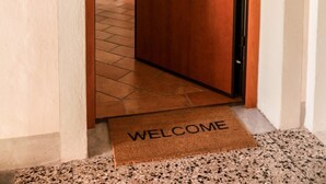 A wooden door with a brass handle, a welcome mat, and a light switch on the wall. - La Casa sul Corso - In the Heart of Foiano della Chiana (Foiano della Chiana)