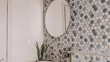 Un baño con un lavamanos blanco, un espejo redondo y un papel tapiz estampado.