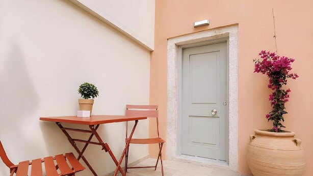 A small outdoor seating area with a table and chairs, a potted plant, and a door.