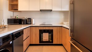 A modern kitchen with wooden cabinets, a built-in oven, a dishwasher, and a refrigerator. - 2-bedroom with Lagoon and Pool View (Bavaro)