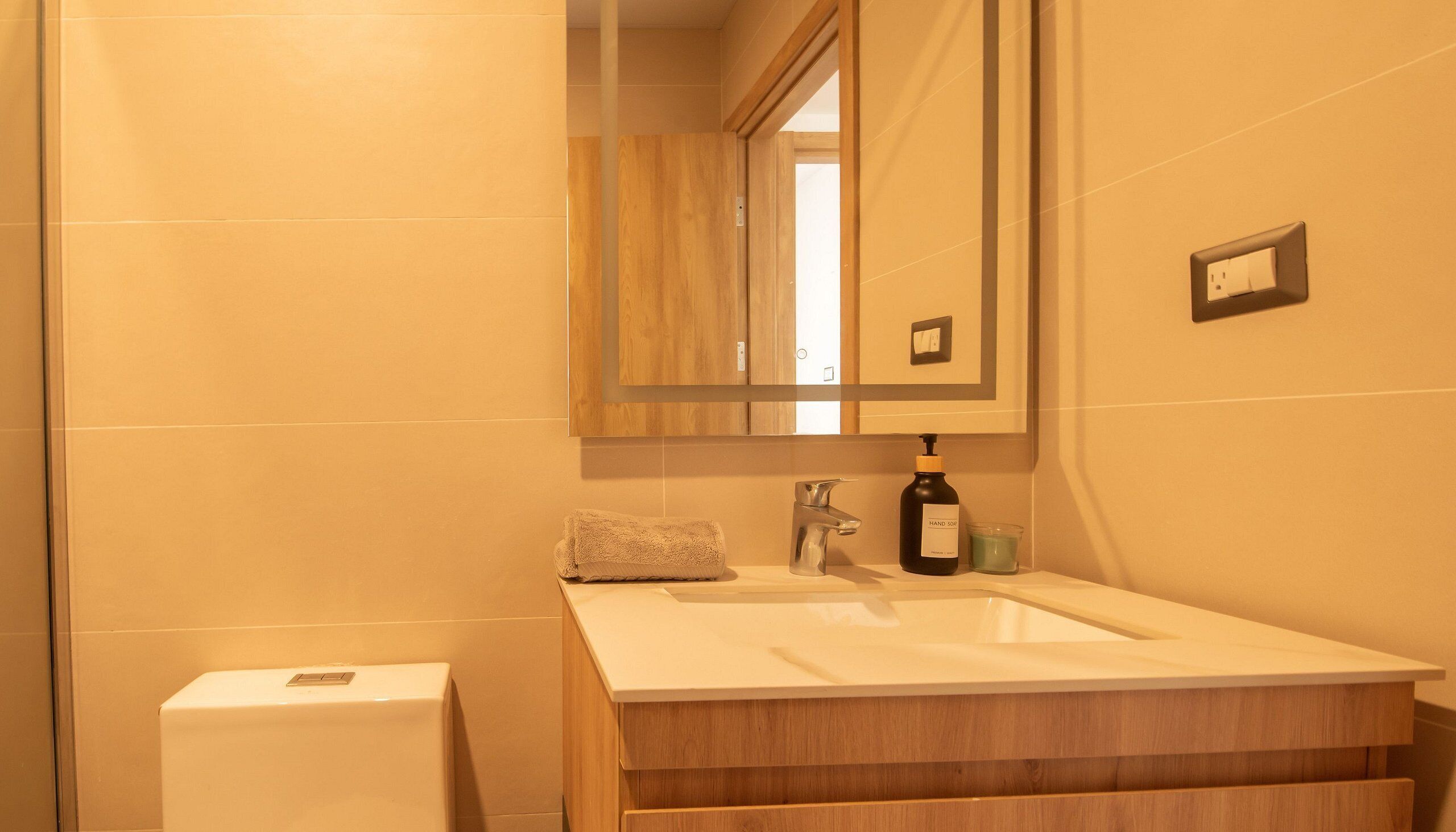 A bathroom with a wooden vanity, a sink, a mirror, a towel, and a soap dispenser.