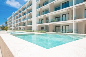 A multi-story hotel with a swimming pool and outdoor seating. - 2-bedroom with Lagoon and Pool View (Bavaro)
