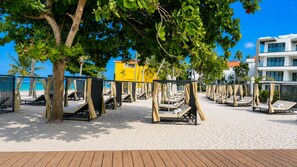 Um resort na praia com espreguiçadeiras sob as árvores, um deck de madeira e vista clara para o oceano.