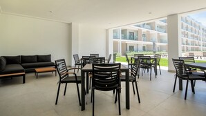 A modern indoor dining area with a sofa and chairs, large windows, and a view of a building. - 2-bedroom with Lagoon and Pool View (Bavaro)