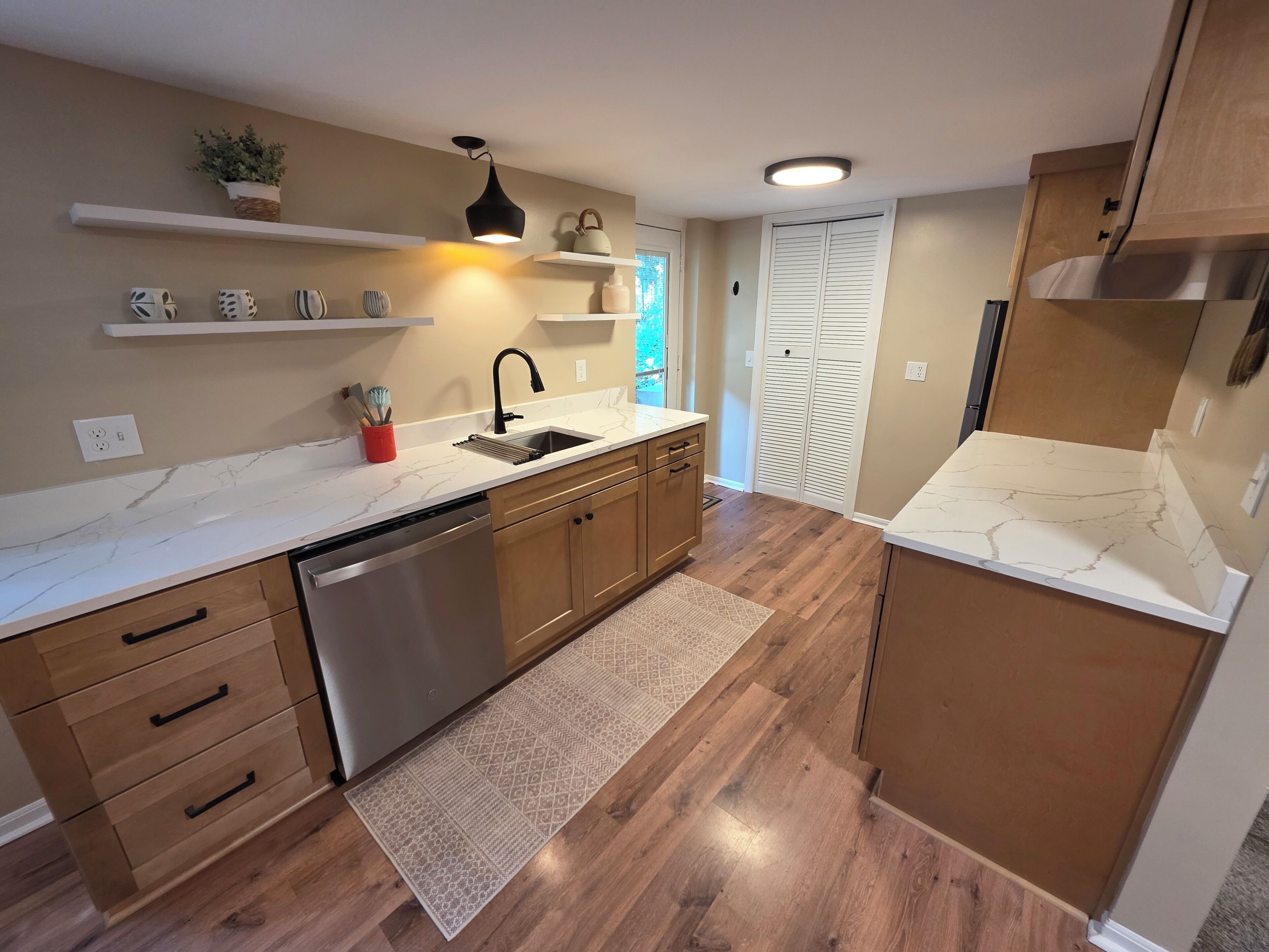 A modern kitchen with wooden cabinets, a stainless steel dishwasher, and a marble countertop.