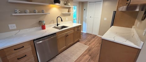 A modern kitchen with wooden cabinets, a stainless steel dishwasher, and a marble countertop.