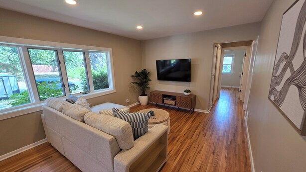 A living room with a beige sofa, a flat-screen TV mounted on the wall, and a wooden floor. - Spacious 5-bedroom house in Bloomington (Minneapolis)