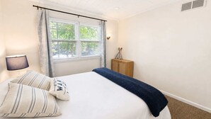 A bedroom with a bed, a nightstand, a lamp, a window with curtains, and a wooden cabinet. - Lakeside Escape With Boat Slip (Rocky Mount)