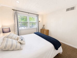 A bedroom with a bed, a nightstand, a lamp, a window with curtains, and a wooden cabinet. - Lakeside Escape With Boat Slip (Rocky Mount)