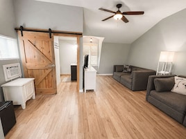 Un espacio habitable estilo loft con puerta de madera, ventilador de techo, sofá, televisor y lámpara.