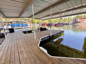 Un muelle de madera cubierto con un bote, una zona de estar techada y vistas a una casa en construcción al otro lado del agua.