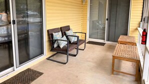 A covered patio with sliding glass doors, a wooden table, and wicker chairs. - Lakeside Escape With Boat Slip (Rocky Mount)