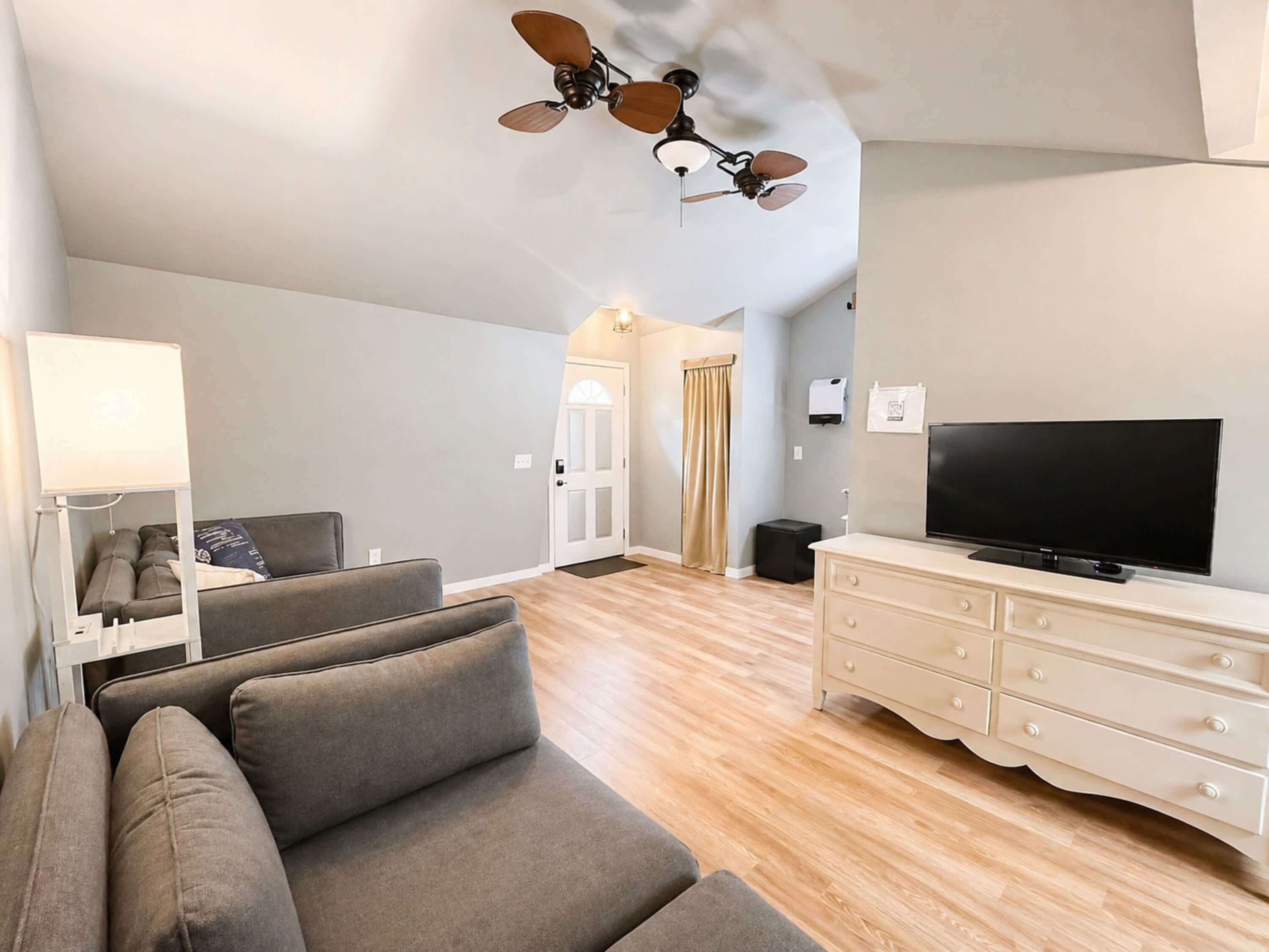 A modern living room with a sofa, TV, ceiling fan, and a light fixture.