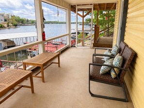 A covered balcony with a wooden table and chairs, overlooking a body of water with boats and a dock. - Lakeside Escape With Boat Slip (Rocky Mount)