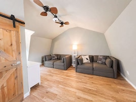 Una habitación estilo loft con techo inclinado, dos sofás grises, una puerta de madera y una lámpara de pie.