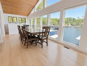 A dining area with a wooden table and chairs, large windows with a view of a body of water and greenery. - Lakeside Escape With Boat Slip (Rocky Mount)