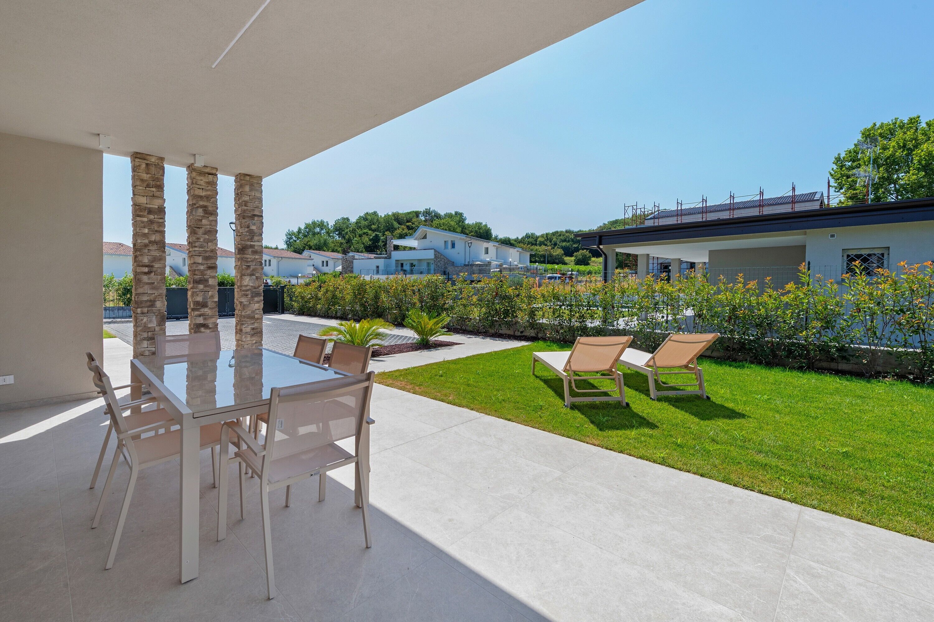 A patio with a glass table and chairs, a grassy lawn, and a view of houses in the background.