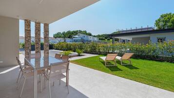 Une terrasse avec une table et des chaises en verre, une pelouse verdoyante et une vue sur les maisons au loin.
