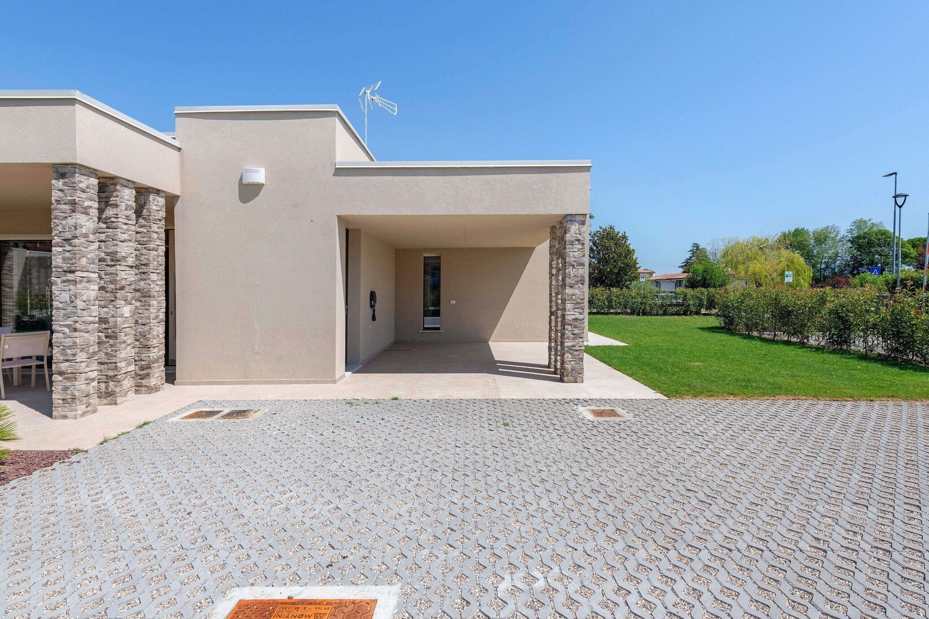 Un bâtiment moderne avec une entrée pavée, des piliers en pierre et un ciel dégagé.