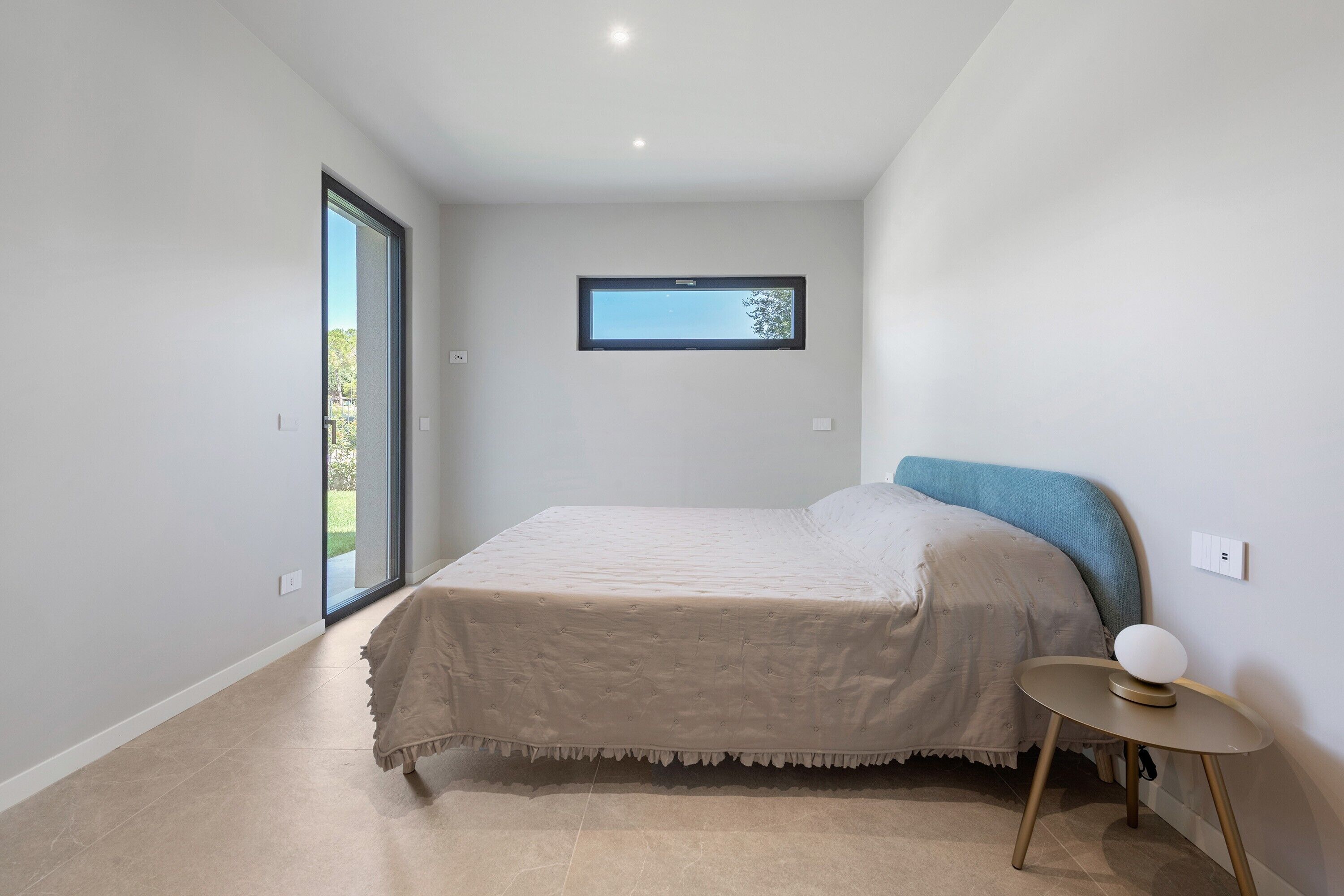 Ein Schlafzimmer mit Bett, einem kleinen runden Tisch mit Lampe, einem Fenster mit Blick und einem Wandfernseher.