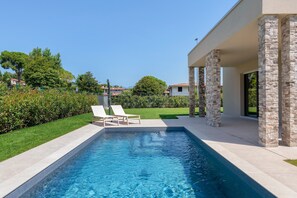 A swimming pool with lounge chairs, stone pillars, and a clear view of the surrounding greenery and houses.