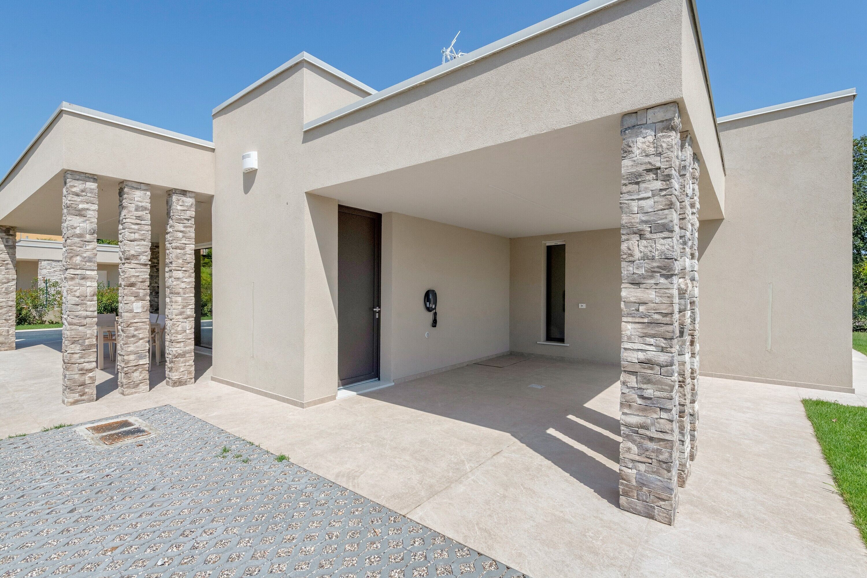 Un edificio moderno con un acceso cubierto, pilares de piedra y cielo despejado.
