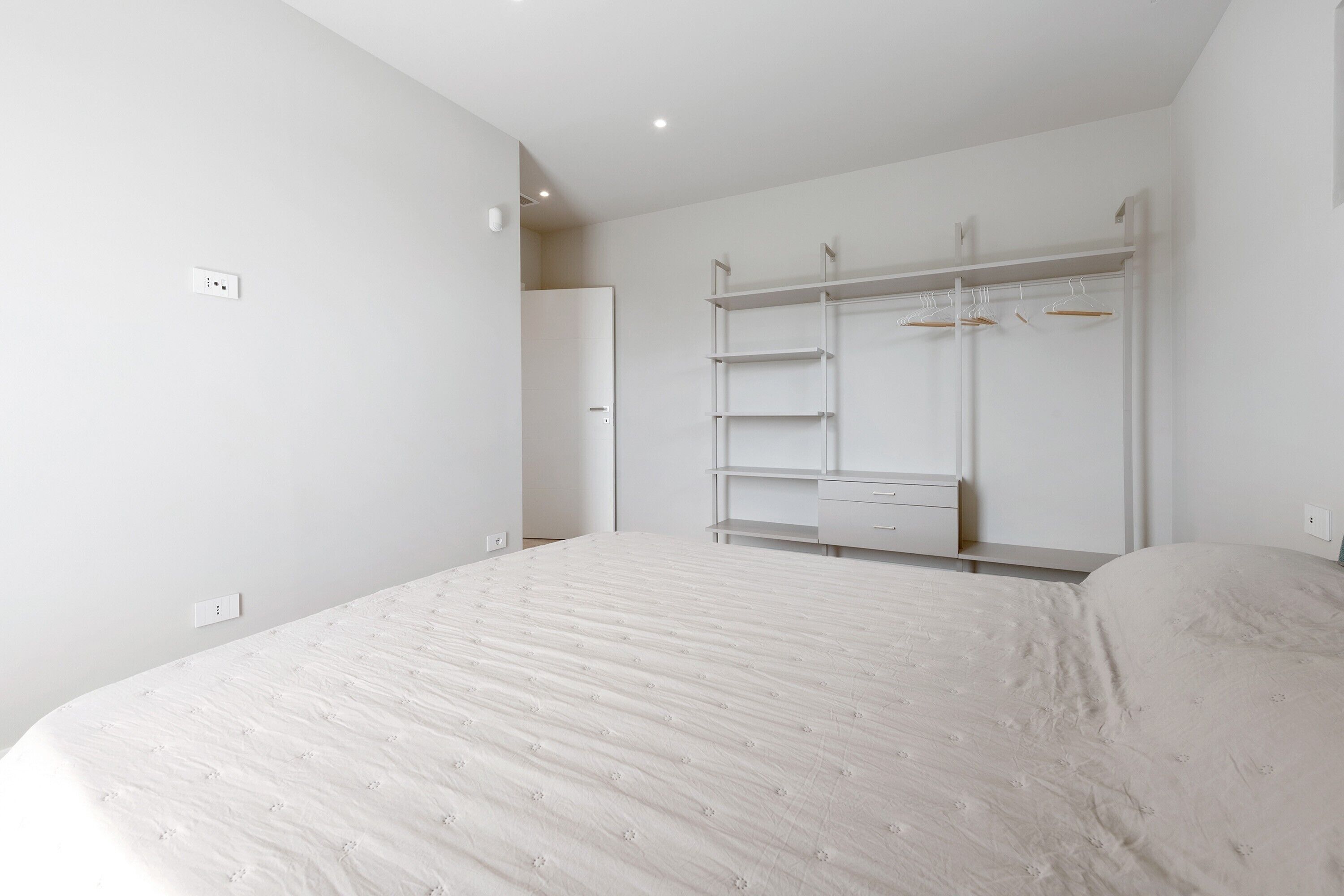 A bedroom with a bed, a wardrobe with multiple shelves and hangers, and a door leading to another room.