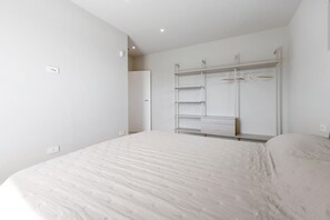 A bedroom with a bed, a wardrobe with multiple shelves and hangers, and a door leading to another room.