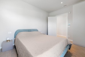 Un dormitorio con cama, mesita de noche, luz en la pared y una puerta.