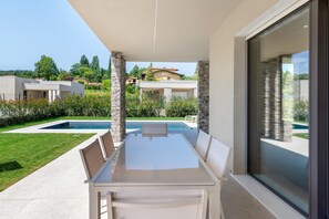 Un espacio moderno para comer al aire libre con piscina, pilares de piedra y vista a casas vecinas.