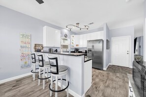Eine moderne Küche mit weißen Schränken, einem Edelstahlkühlschrank und einer Bar mit Hockern.
