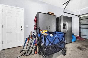 Eine Garage mit weißer Tür, einem Vorratsraum, einem Kühlschrank und einem blauen Rollwagen.
