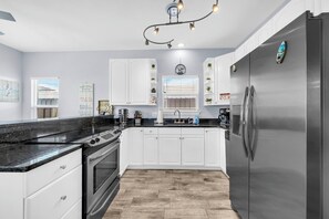 Eine moderne Küche mit weißen Schränken, einem Edelstahl-Kühlschrank, einer schwarzen Arbeitsplatte und einem Holzboden.