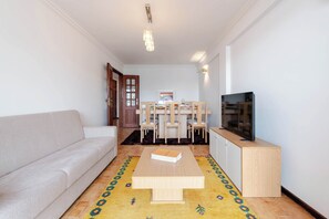 A living room with a sofa, a coffee table, a dining table with chairs, a television, and a cabinet. - Bright & Spacious Flat with Balcony by HostWise (Matosinhos)