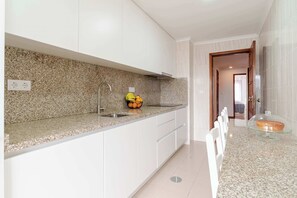 A modern kitchen with granite countertops, white cabinets, and a stainless steel sink. - Bright & Spacious Flat with Balcony by HostWise (Matosinhos)