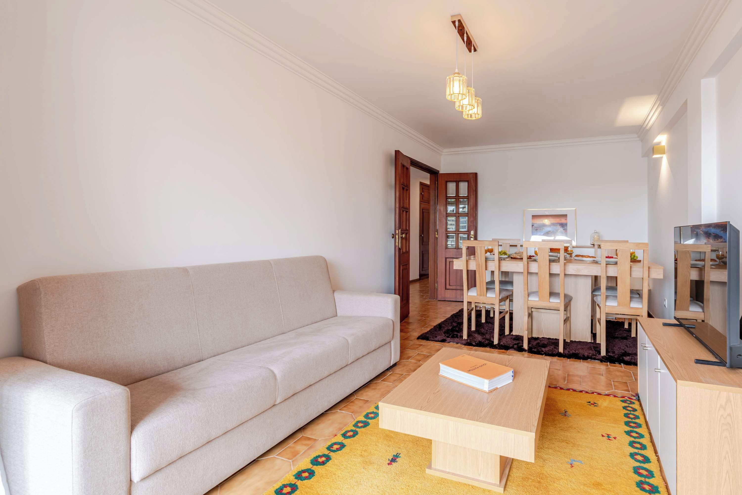 Una sala de estar con sofá, una mesa de centro, un comedor con sillas y una mesa, y una zona de cocina con armarios.