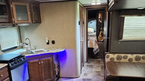 Une cuisine compacte équipée d’un évier, d’une cuisinière et de placards, qui donne sur une chambre avec un lit et une fenêtre.