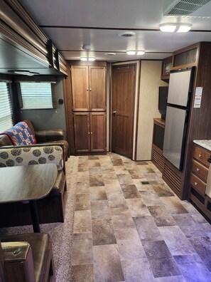 Ein kompaktes Wohnmobil-Interieur mit einer Küchenzeile, einer Sitzecke mit gemustertem Kissen und einem gefliesten Boden.