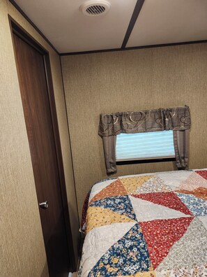 Ein Schlafzimmer mit Holztür, einem fenster mit Vorhängen und einer mehrfarbigen Steppdecke auf dem Bett.