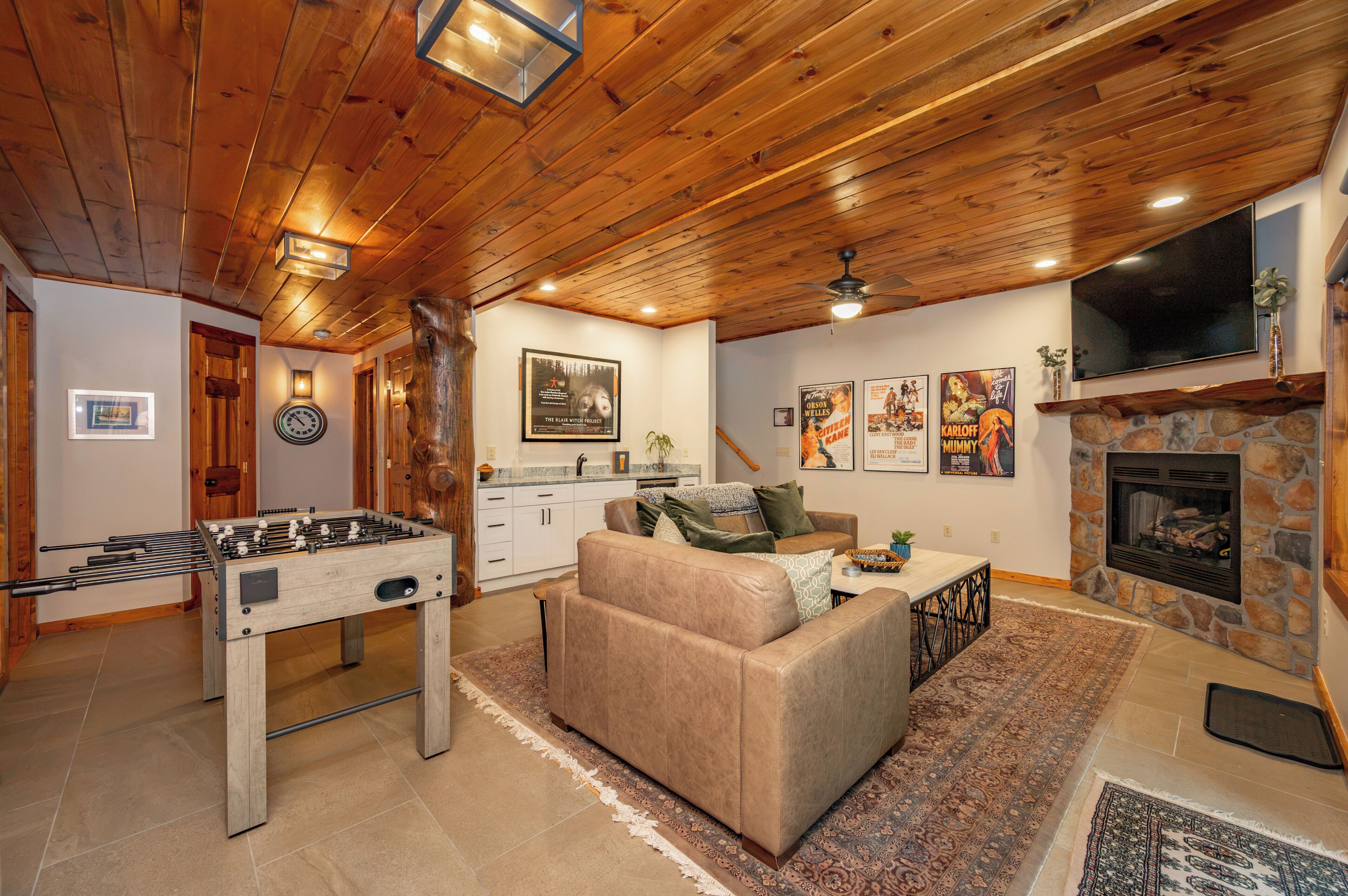 A cozy living room with a foosball table, a stone fireplace, and a television mounted on the wall.