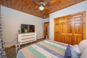 Ein Schlafzimmer mit Holzboden, Deckenventilator, Bett mit gestreifter Bettdecke, weißem Schminktisch und Holzschrank.