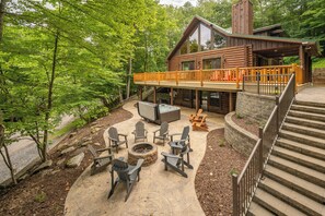 Eine Blockhütte mit einer Terrasse, Sitzgelegenheiten im Freien, einer Feuerstelle und einer Steintreppe.