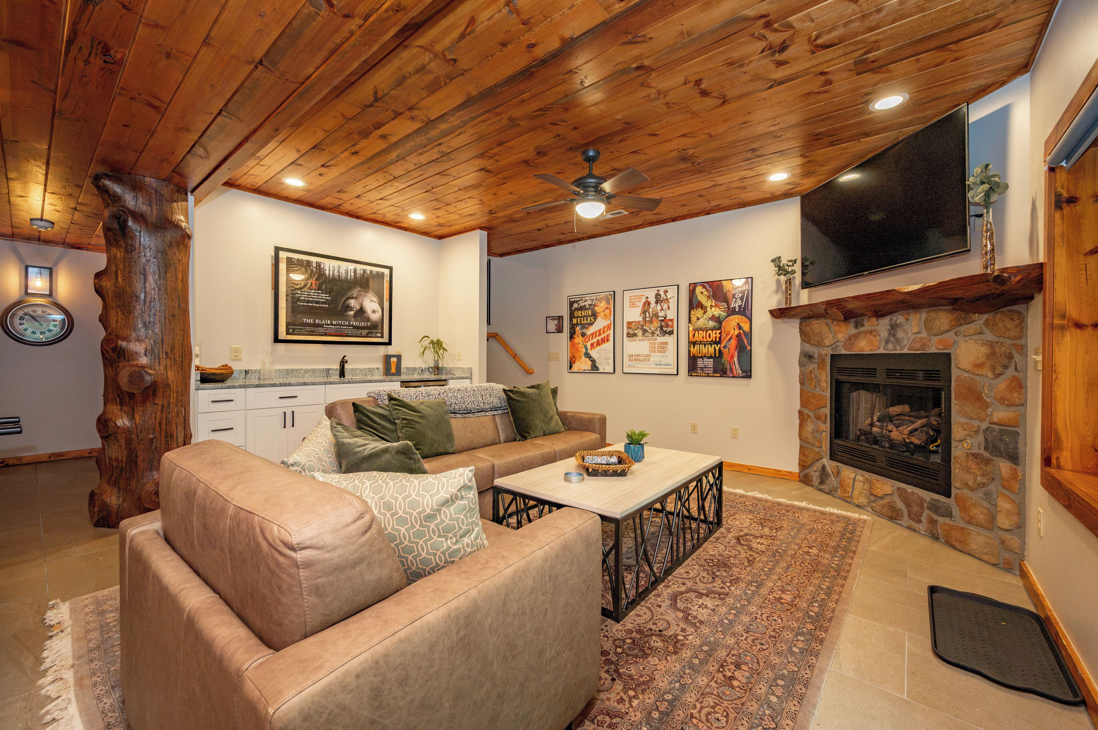 A cozy living room with a stone fireplace, a wooden ceiling, and a television mounted above it.