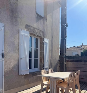 Eine Terrasse mit Tisch und Stühlen, ein Fenster mit Fensterläden und eine Gebäudefassade.