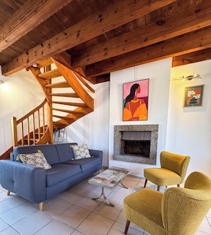 Ein Wohnzimmer mit blauem Sofa, gelben Sessel, Holztreppe, Kamin und Kunstwerken an den Wänden.