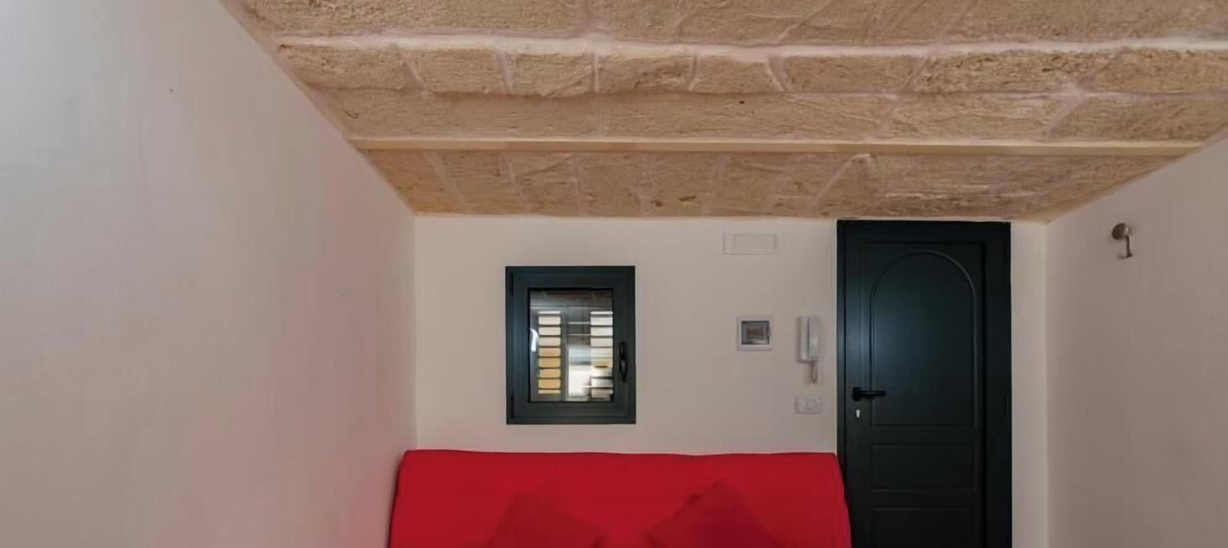 A room with a red sofa, a black door, and a small window with blinds.