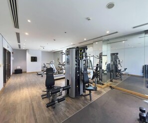 Un gimnasio con diversas máquinas de ejercicio, un espejo grande y suelo de madera.