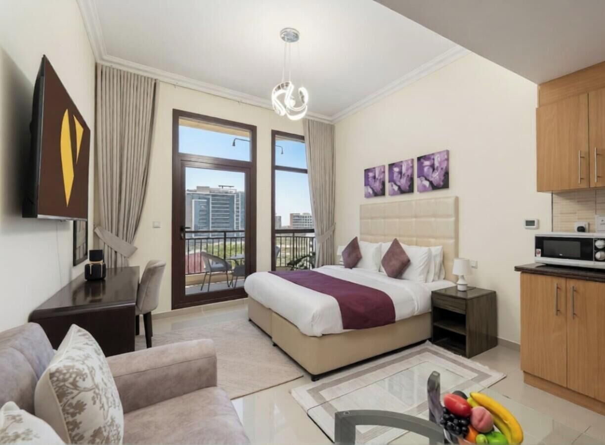 Een hotelkamer met een bed, een bureau, een stoel, een bank, een balkon met uitzicht en een kitchenette.