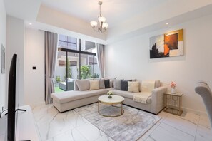 A modern living room with a sectional sofa, a round coffee table, and a painting on the wall. - Vogue, Wadi Al Safa Villa The Fields Elie Saab (Wadi Al Safa)