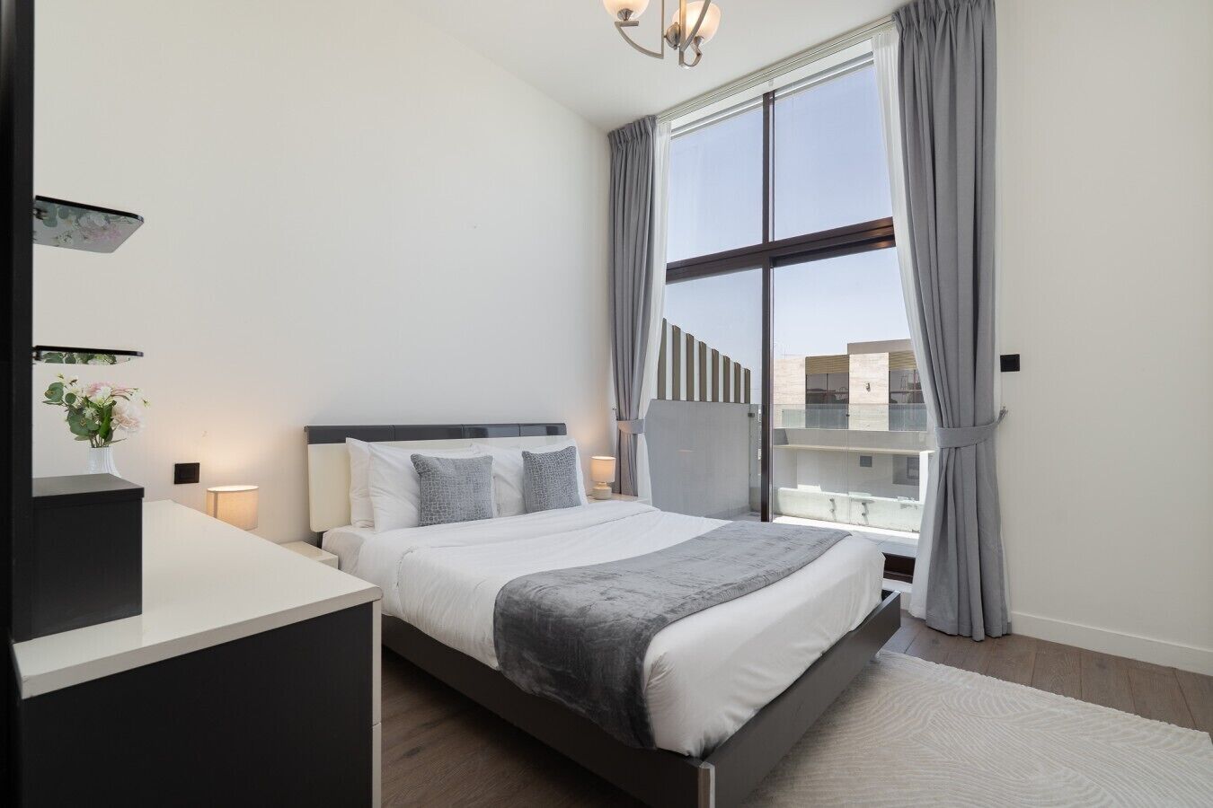 Ein modernes Schlafzimmer mit einem Bett, Nachttischen, einem Schreibtisch und einem großen Fenster mit Vorhängen.